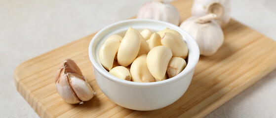 Wooden board with fresh garlics and bowl of cloves on white background, closeup