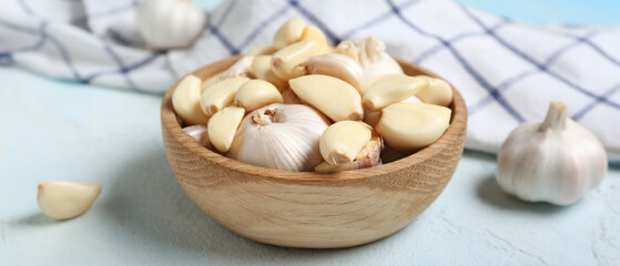 Wooden bowl with fresh garlics on light blue background, closeup