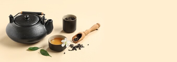 Teapot with cup, wooden scoop and dry tea leaves on beige background with space for text