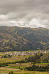 Fototapeta premium The town of Sora as seen from the Pena Parida hill, surrounded by farm lands, under an overcast sky, in the eastern Andean mountains of central Colombia.