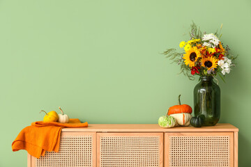 Wooden cabinet with bouquet of autumn flowers and pumpkins near green wall