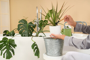 Young woman fluffing soil of plant in bathroom, closeup