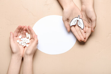 Hands of woman and child with paper lungs, pills and blank card on beige background