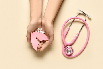 Female hands with paper lungs, pills and stethoscope on beige background