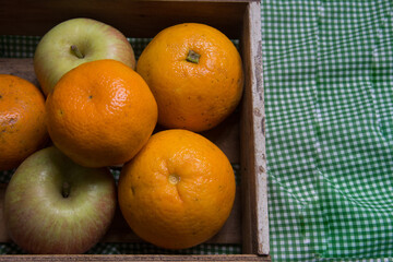 Oranges ,  tangerines and apples in a wooden box on a green tablecloth
