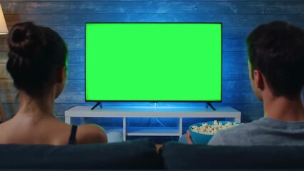 Back View of Couple Eating Popcorn While Watching Green Screen TV in Cozy Living Room - Powered by Adobe