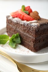 Piece of delicious chocolate cake with strawberry, almonds and mint on table, closeup