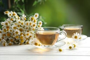 Aromatic tea in glass cups and chamomile flowers on white wooden table, closeup