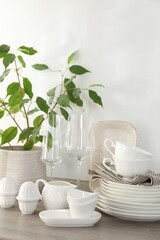 Different clean white dishware, glasses and houseplant on counter in kitchen, closeup