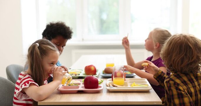 Little kids eating lunch at wooden table in school canteen