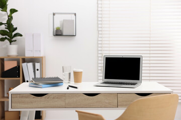 Stylish workplace with laptop, coffee and stationery on white table in office