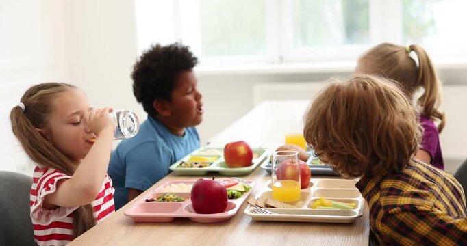 Little kids eating lunch at wooden table in school canteen