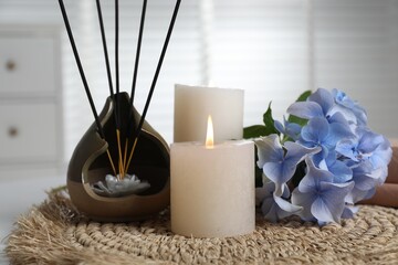 Spa composition of holder with incense sticks, burning candles and flowers on wicker mat indoors,...
