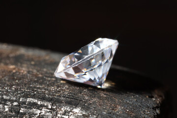 One shiny diamond on burnt piece of wood against black background, macro view
