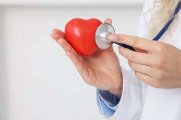Pediatrician checking heartbeat of heart model in clinic, closeup