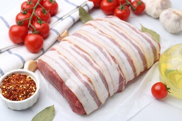 Piece of raw beef meat, tomatoes and spices on white table, closeup