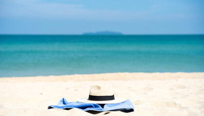 Obraz premium Striped blue towel folded near straw hat on sandy beach , holiday, color