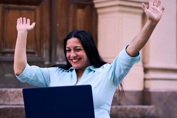 Beautiful mature Latina woman working on her laptop outdoors at home, smiling, energetic, and very...