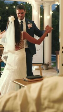 Vertical video: Groom is passing guests under string lights and taking bride's hand for first dance