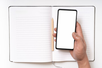 Hand hold smartphone above notepad with pen on workspace table