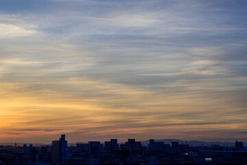 Fototapeta premium 神戸市の夜明け、ビルの隙間から太陽が昇り辺りはオレンジ色に染まりビルはシルエットに浮かぶ。