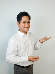 Confident Professional Man Gesturing Open Hand for Presentation or Welcome. A cheerful young Asian...