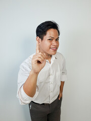 Confident man in a formal white shirt smiling and pointing upward with one finger raised,...