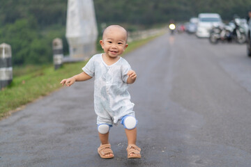 Happy baby learning to walk on road wearing knee pads