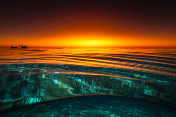 A dramatic half-underwater view of glowing sunset skies with a shipwreck silhouette and reef below...