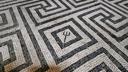Herculaneum, Italy - 9 January 2025. Trident motif within a labyrinthine mosaic floor, possibly referencing Neptune, in an ancient Roman bath or villa.