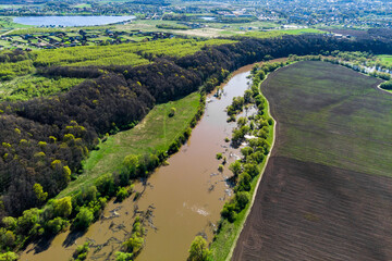 Terrain with a river flowing past fields and dense forest, aerial view from above