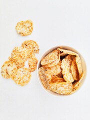 Tempeh chips in a white bowl on a white background. Top of view. 