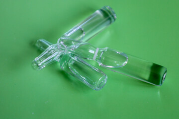 ​A group of clear glass ampoules of various sizes lies crosswise on a solid green background....
