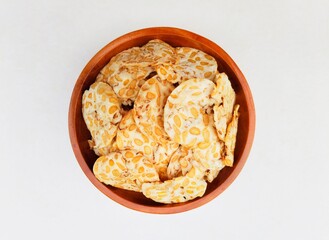 Tempeh chips in a wooden plate on a white background. 