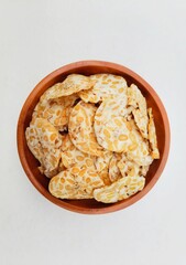 Tempeh chips in a wooden plate on a white background. Top of view. 