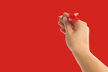 A hand grips a red dart poised to be thrown at a target