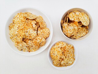 Tempeh chips in white plates and a white bowl on a white background. 