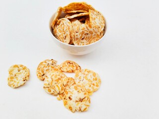 Tempeh chips in a white bowl on a white background. High angle view. 