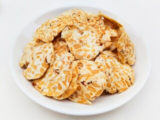 Close-up of tempeh chips in a white plate on a white background. 