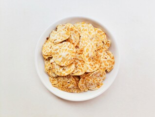 Tempeh chips in a small white plate on a white background. Top of view. 