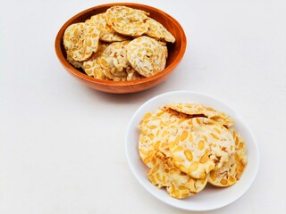 Tempeh chips in a small white plate and a wooden plate on a white background. High angle view. 