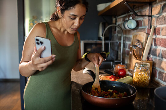 Young woman cooking healthy meal while checking recipe on phone