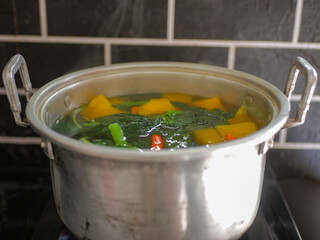 Spinach and pumpkin clear soup in a pot with red chili, traditional Indonesian healthy vegetable dish. Sayur bening bayam dan labu, fresh, delicious
