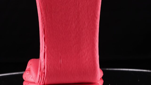 A close-up shot of a vibrant pink slime substance flowing and pooling on a dark surface
