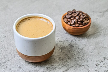 Close up view of hot cappucino in the ceramic mug or glass with coffee beans on the little or small wooden bowl or plate. scattered. grey or gray cement as background.