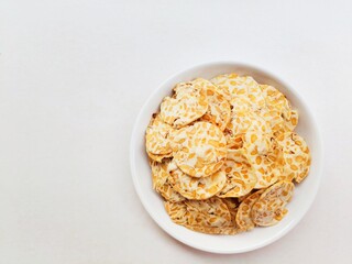 Tempeh chips in a white plate on a white background. Top of view. 