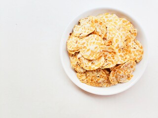 Tempeh chips in a white plate on a white background. Top of view. 