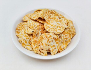 High angle view of tempeh chips in a white plate on a white background. 