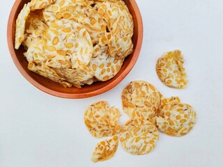 Directly above shot of tempeh chips in a wooden plate on a white background. Top of view. 