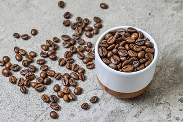 Close up view roasted coffee beans in the ceramic glass or mug. Little, mini. Isolated on gray or gray cement background. Scattered.